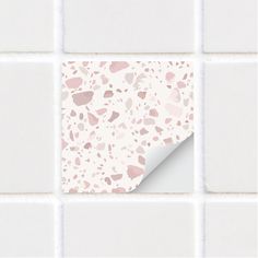 a white tiled wall with pink and grey spots on it's surface, as seen through a hole in the paper