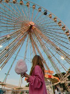 a girl holding cotton candy in front of a ferris wheel