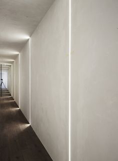 an empty hallway with white walls and wooden floors is lit by light coming from the ceiling