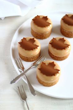 small desserts are arranged on a white plate with silver utensils and forks