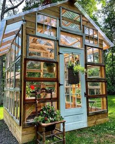 a small greenhouse with lots of windows and plants in the front, surrounded by greenery