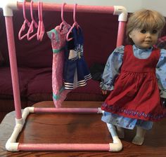 a doll is standing next to a rack with clothes hanging from it's hooks