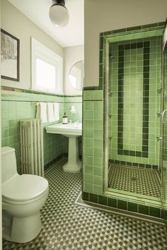 a green tiled bathroom with a toilet, sink and shower stall in the middle of the room