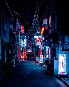 an alley way with neon signs and buildings lit up at night