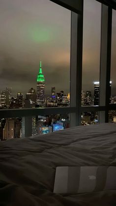 a bed in a room with a view of the city at night and green lights