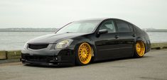 a black car with yellow rims parked on the side of the road near water