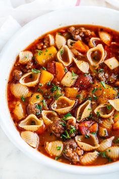 a white bowl filled with pasta and meat soup on top of a marble countertop