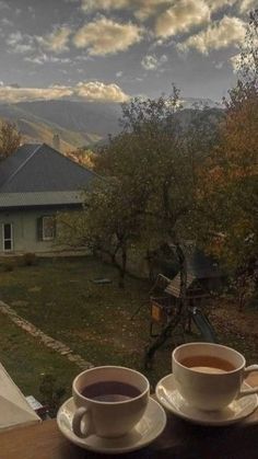 two cups of coffee sitting on top of a wooden table in front of a house