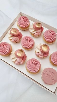 cupcakes with pink frosting and gold decorations in a box