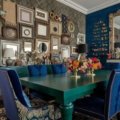 a dining room table with blue chairs and pictures on the wall in front of it