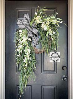 a wreath with white flowers and greenery hangs on the front door's black door