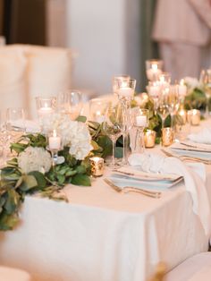 the table is set with white plates and silverware, candles and flowers in vases