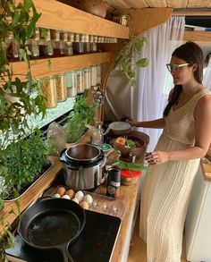 a woman standing in front of a stove top next to pots and pans filled with food