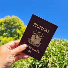 a person holding up a passport in front of some bushes and trees on a sunny day