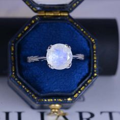 an oval shaped white stone ring in a blue velvet box with gold trimmings