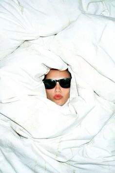 a woman wearing sunglasses hiding under a blanket