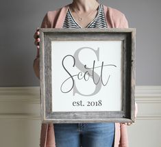 a woman holding up a framed sign with the word scott in cursive font