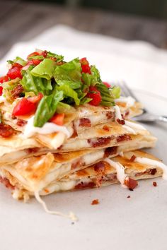 a stack of quesadillas with lettuce, tomatoes and bacon on top