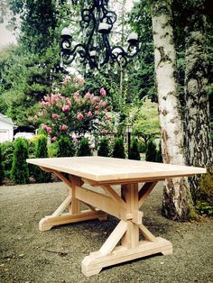 a wooden table sitting next to a tree in front of a light fixture and pink flowers