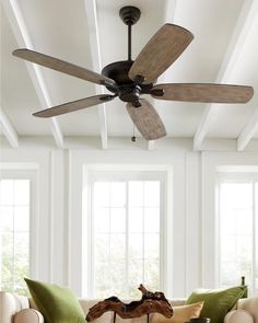 a living room filled with furniture and a ceiling fan in front of two large windows