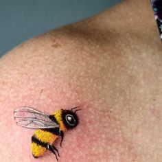 a small yellow and black bee tattoo on the back of a woman's shoulder