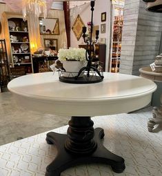 a white table with black legs and a flower pot on top, in a store