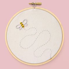 a white embroidered wall hanging with a yellow and black bee on it's side