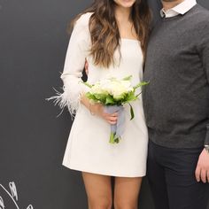 a man and woman standing next to each other with flowers in front of a chalkboard