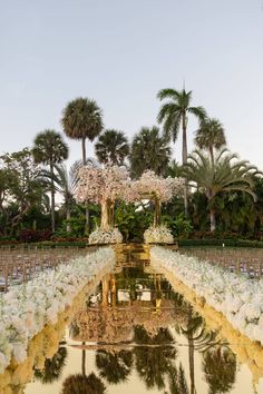 an outdoor ceremony setup with white flowers and greenery in the middle, surrounded by palm trees