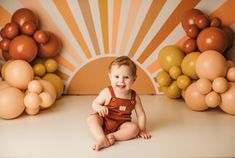 a baby sitting on the floor in front of some balloons and smiling at the camera