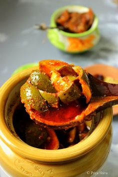 a wooden spoon full of pickles on top of a yellow pot filled with sauce