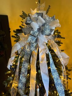 a decorated christmas tree with white and blue ribbons on it's top, lit by candles