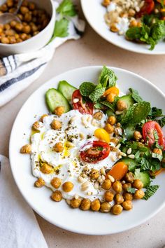 two white plates filled with food on top of a table next to bowls of chickpeas