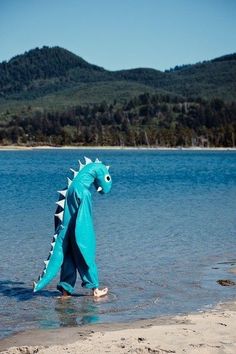 a blue dragon is standing in the water at the edge of a lake with mountains in the background