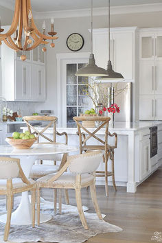 a dining room table with chairs and a bowl of fruit on it in front of a clock