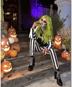 a woman with green hair and makeup sitting on steps in front of carved pumpkins