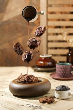 chocolate donuts being drizzled with syrup on a wooden table next to other desserts