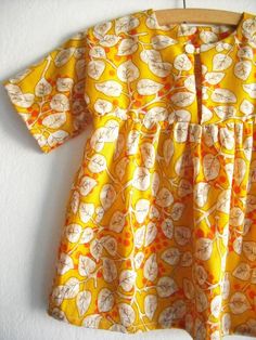 a yellow dress with orange and white flowers on it hanging from a wooden hanger