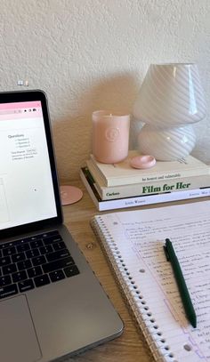 an open laptop computer sitting on top of a wooden desk next to a stack of books