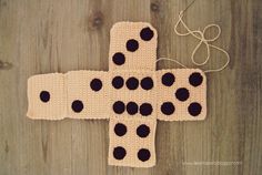 a crocheted cross with black dots on it sitting on top of a wooden floor