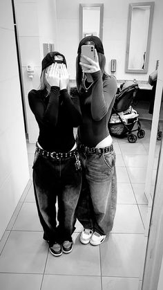 two women taking pictures in the mirror with their cell phones while standing next to each other