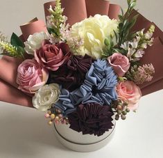 a bouquet of flowers in a white vase on a table with pink and purple ribbons