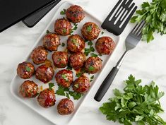 meatballs on a plate with parsley next to a knife and fork