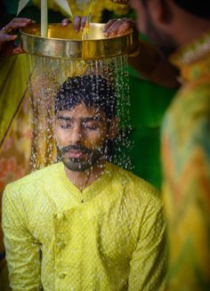 a man is washing his face with water from a metal bowl on top of him