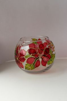 a glass vase with red flowers painted on the side and green leaves in the middle