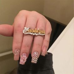 a woman's hand with pink and gold nail art on it, holding onto her name plate