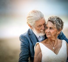 an older couple embracing each other in front of the camera, with one woman wearing a white dress