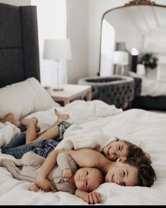 two young children laying on top of each other on a white bed in a bedroom