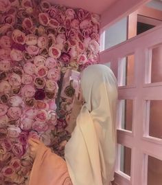 a woman in a hijab is looking at flowers on the wall behind her