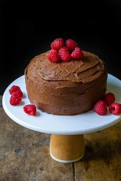 a chocolate cake topped with raspberries on top of a white plate and wooden stand